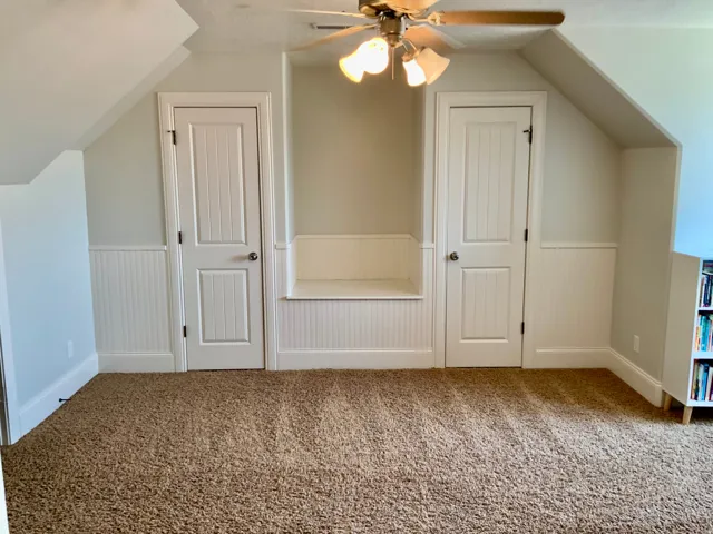 Carpeted room featuring a built-in bench, two paneled doors, wainscoting, and a ceiling fan with light fixture