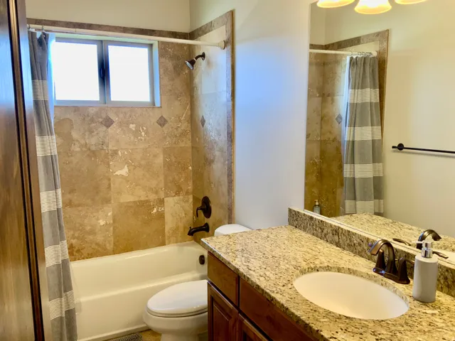 Bathroom featuring a built-in tub with a tiled surround, a vanity with a stone countertop, an undermount sink, and a framed mirror
