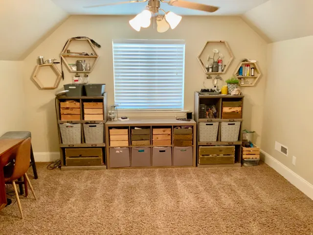 Carpeted room with sloped ceilings and a central window with horizontal blinds