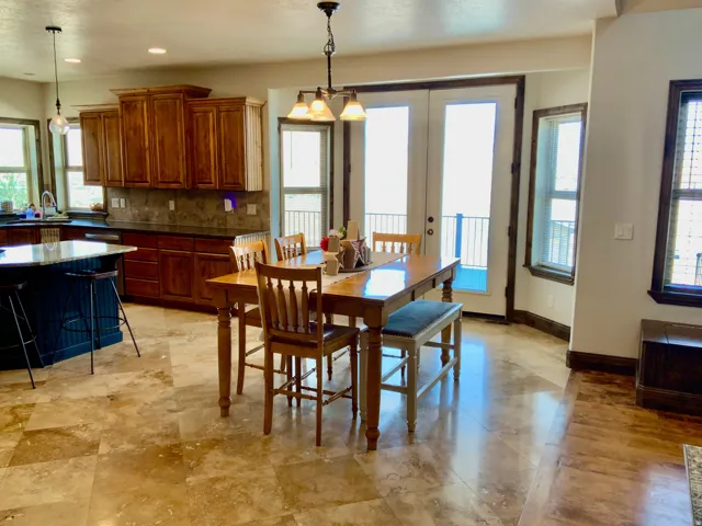 Open-concept dining area featuring light-toned tile flooring, direct outdoor access via double glass doors, a multi-light chandelier, and wood-framed windows