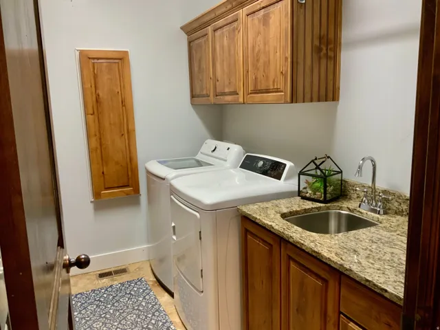 Laundry area featuring extensive wood cabinetry, a utility sink with a stainless steel basin, and a granite-finish countertop