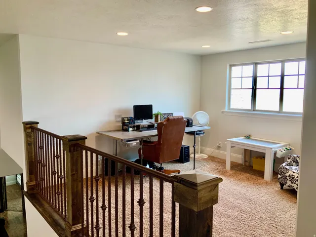 Carpeted loft area featuring a window with grid panes, recessed lighting, and a dark wood and metal baluster railing
