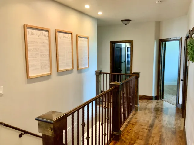 Upper-level hallway with wood-finish flooring, dark wood trim, and a metal baluster railing