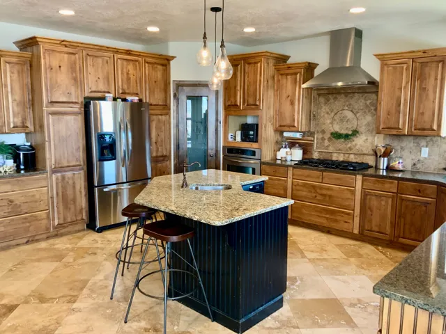 Gourmet kitchen featuring wood cabinetry, stone countertops, stainless steel appliances, a center island with a sink, and tile flooring