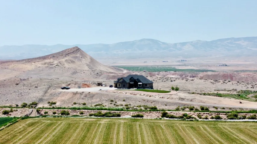 Expansive property featuring a contemporary residence with a dark roof and light-toned siding, set against a backdrop of rolling hills and distant mountains