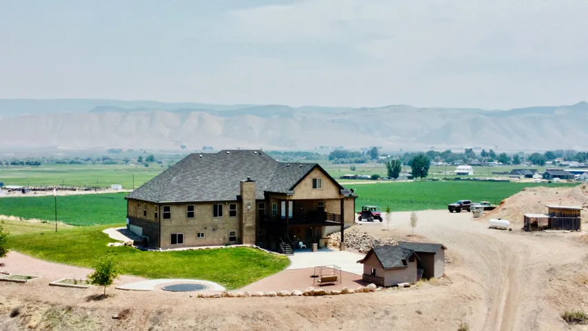 Large residential structure featuring multiple levels, an attached balcony, a stone chimney, a paved patio area, and a separate small outbuilding