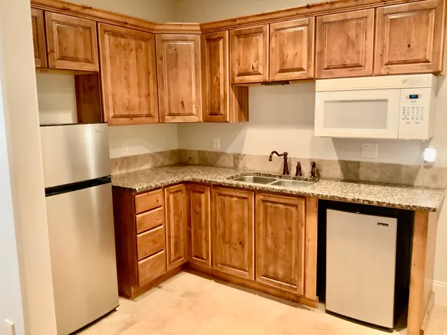 Compact kitchen featuring wood cabinetry, granite countertops with a stone backsplash, and a double basin sink with an oil-rubbed bronze faucet