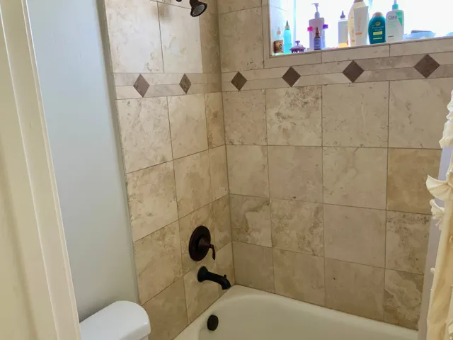 Bathtub with tiled surround featuring decorative diamond accents and bronze-finish fixtures