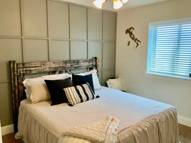 Bedroom featuring a decorative accent wall with panel molding and a window with blinds