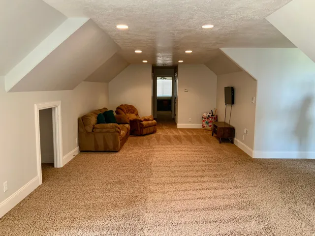 Carpeted room featuring sloped ceilings, recessed lighting, white baseboards, and a doorway leading to an interior space