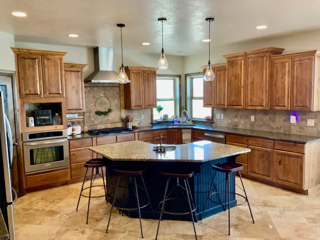 Spacious kitchen featuring a central hexagonal island with seating, extensive wood cabinetry, granite countertops, and stone-look tile flooring