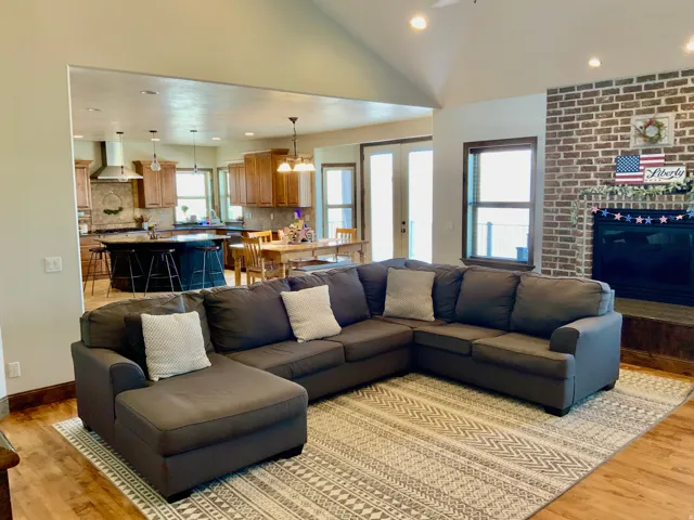 Open-concept living area featuring wood-finish flooring, vaulted ceilings, and a brick-faced fireplace