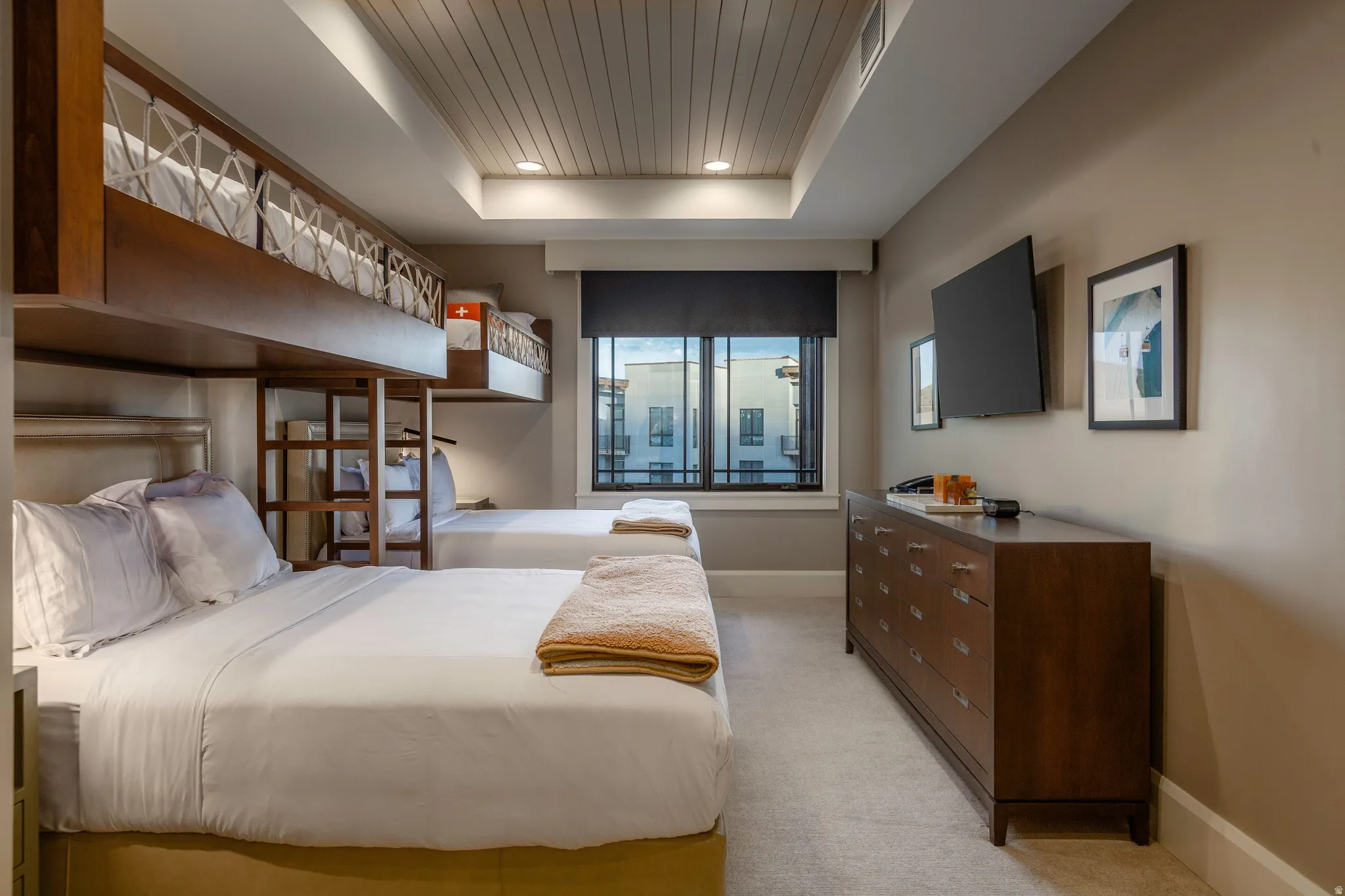 Efficiently designed sleeping area featuring a custom built-in bunk bed system, recessed lighting, a window with a roller shade, light-toned carpeting, and a long wood-finish dresser