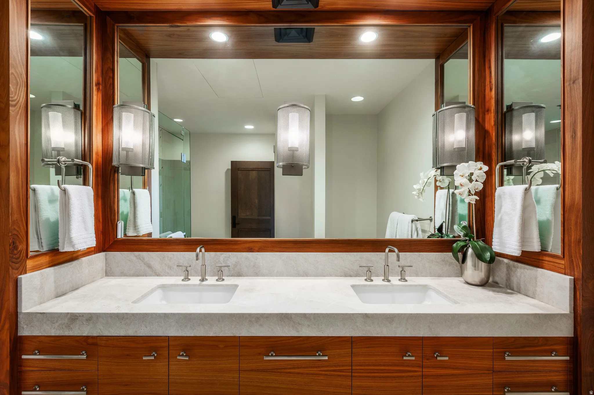Dual vanity featuring a large framed mirror, stone countertop, integrated rectangular sinks, and wood-finish cabinetry with brushed nickel hardware