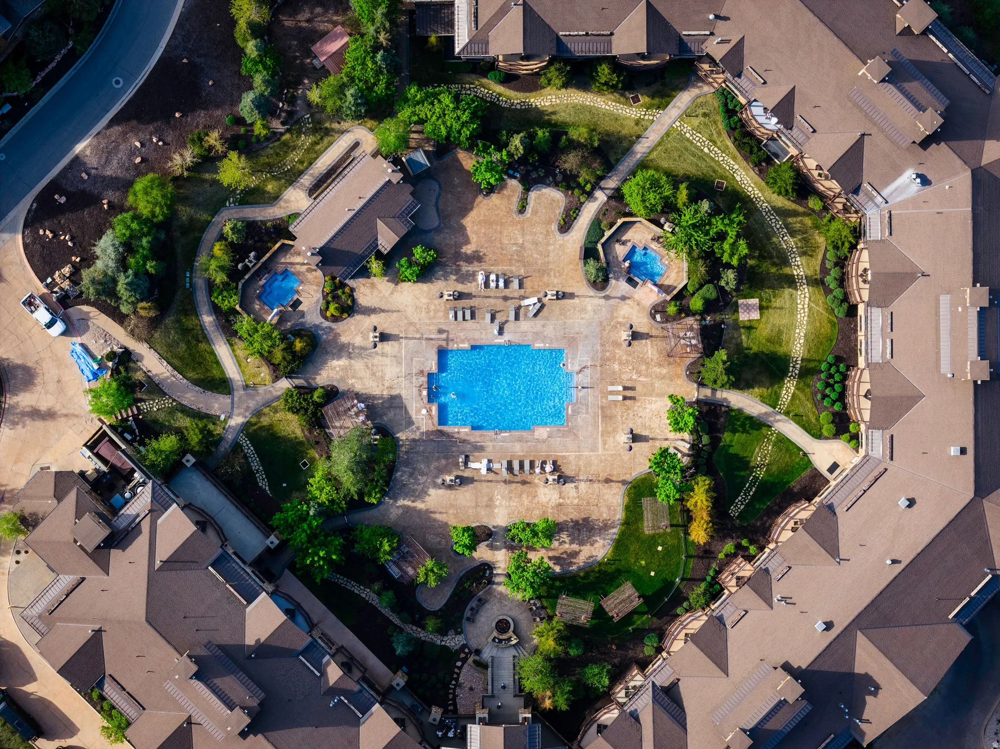 Central swimming pool surrounded by a large hardscaped patio area with multiple seating zones