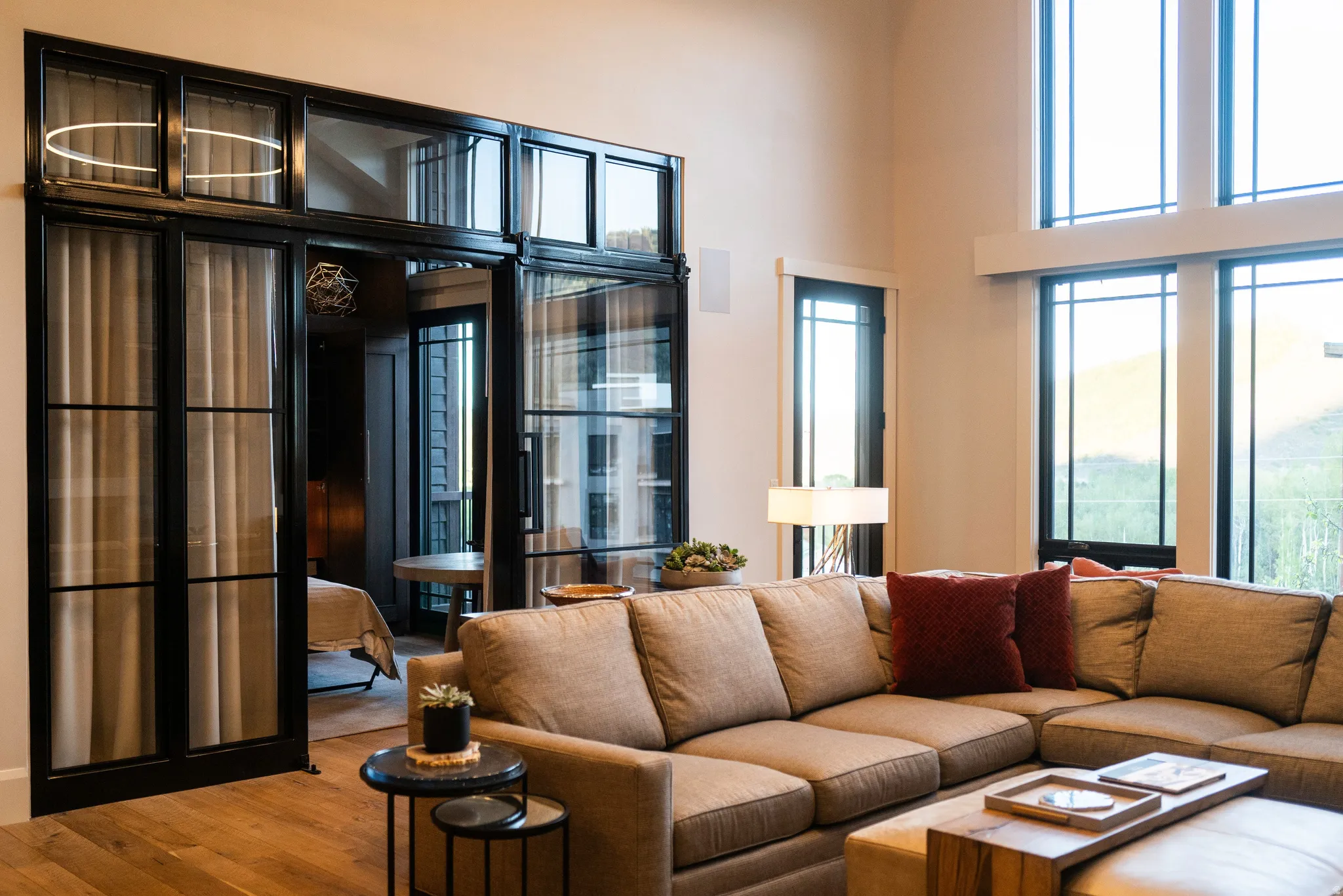 Living area featuring tall windows, black-framed glass doors, wood-finish flooring, and light-toned walls