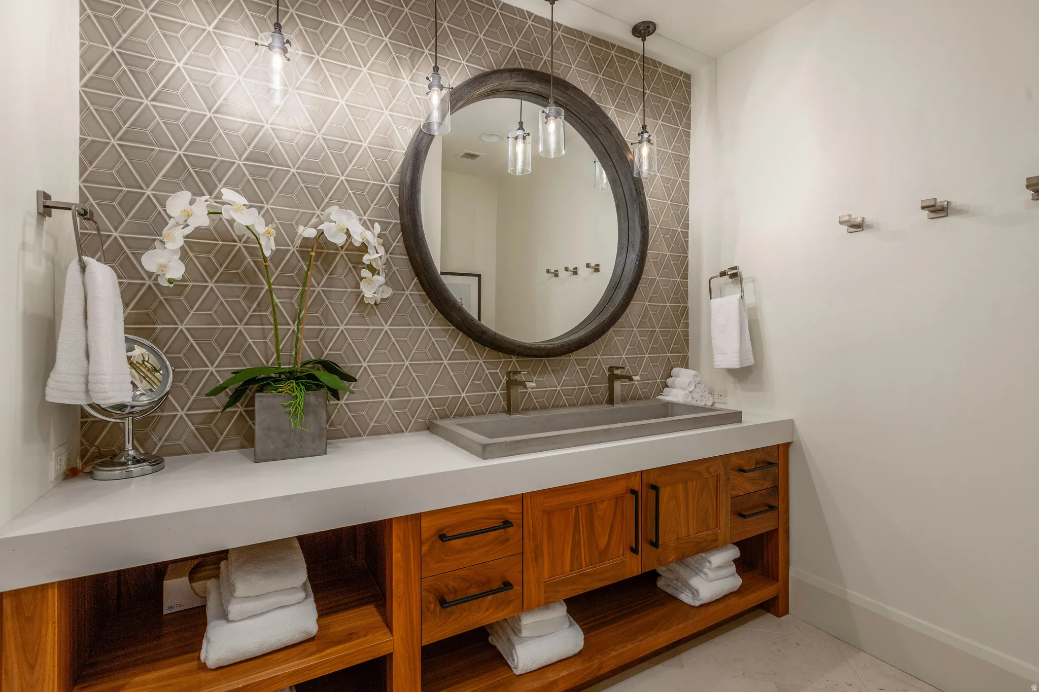 Bathroom featuring a geometric tiled accent wall, round mirror, and two pendant light fixtures