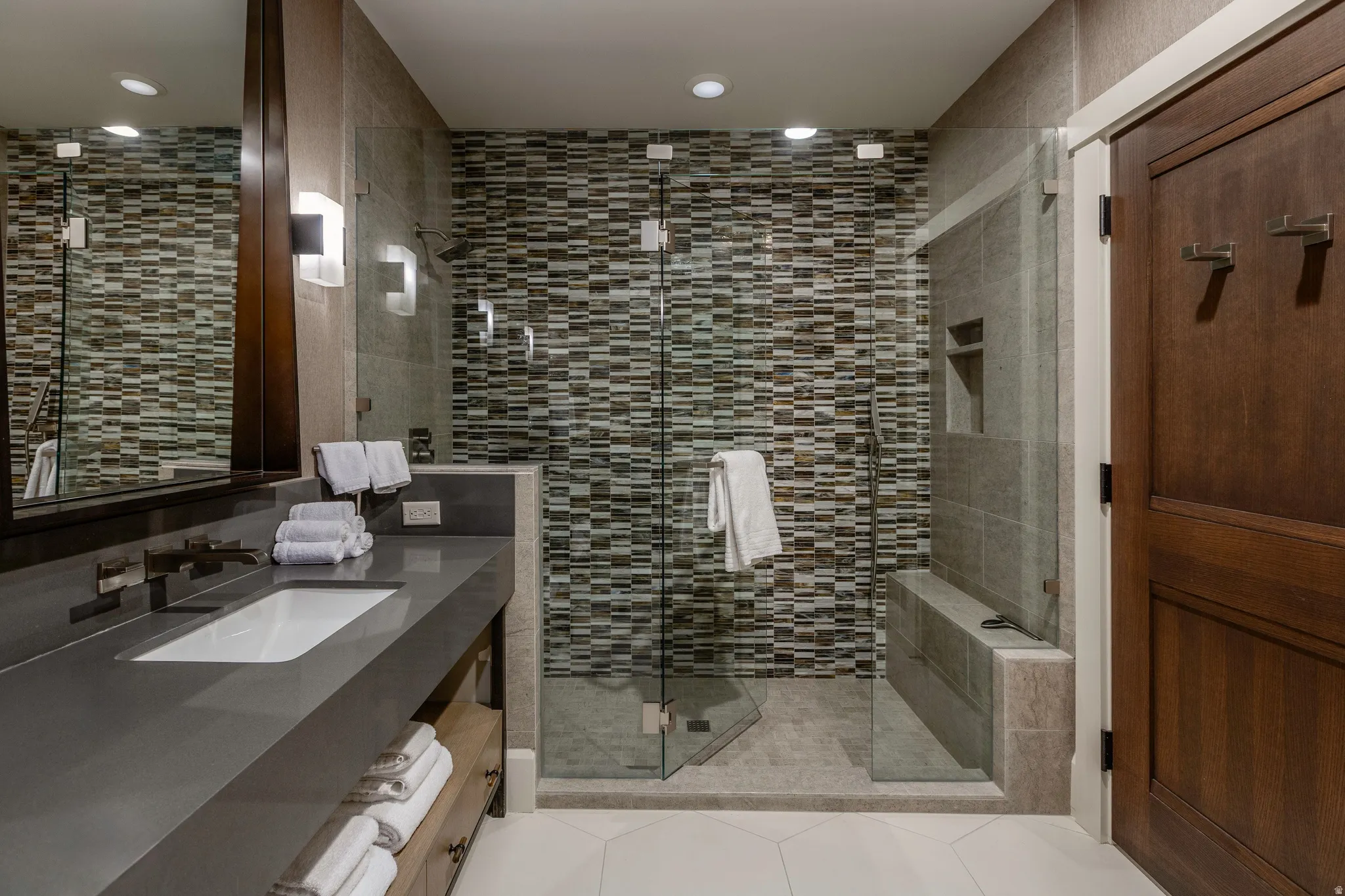 Bathroom featuring a glass-enclosed shower with mosaic tile detailing, a built-in shower bench, and a recessed niche