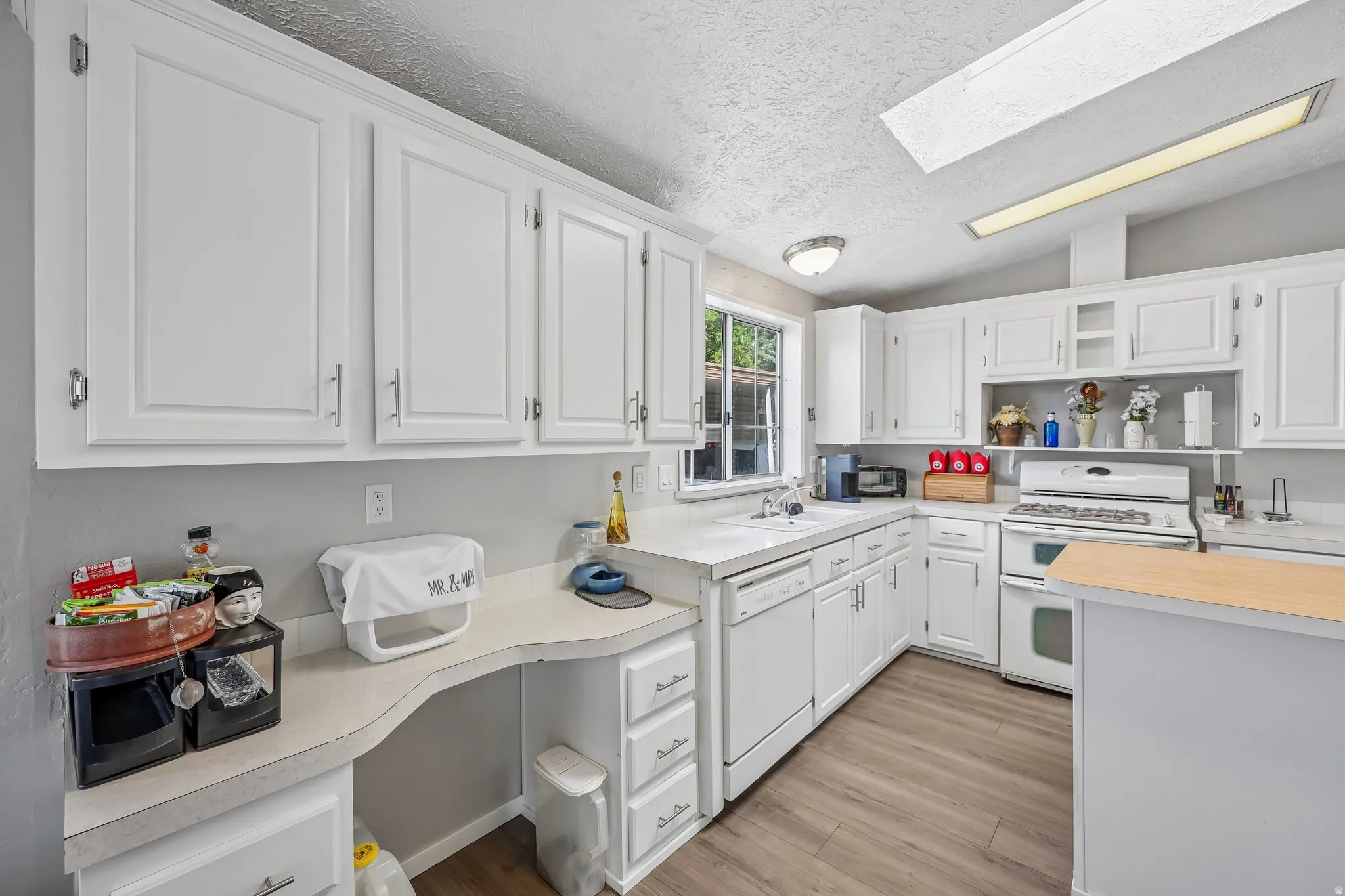 Kitchen featuring white cabinetry, light gray walls, wood-finish flooring, a built-in desk area, and a window above the sink