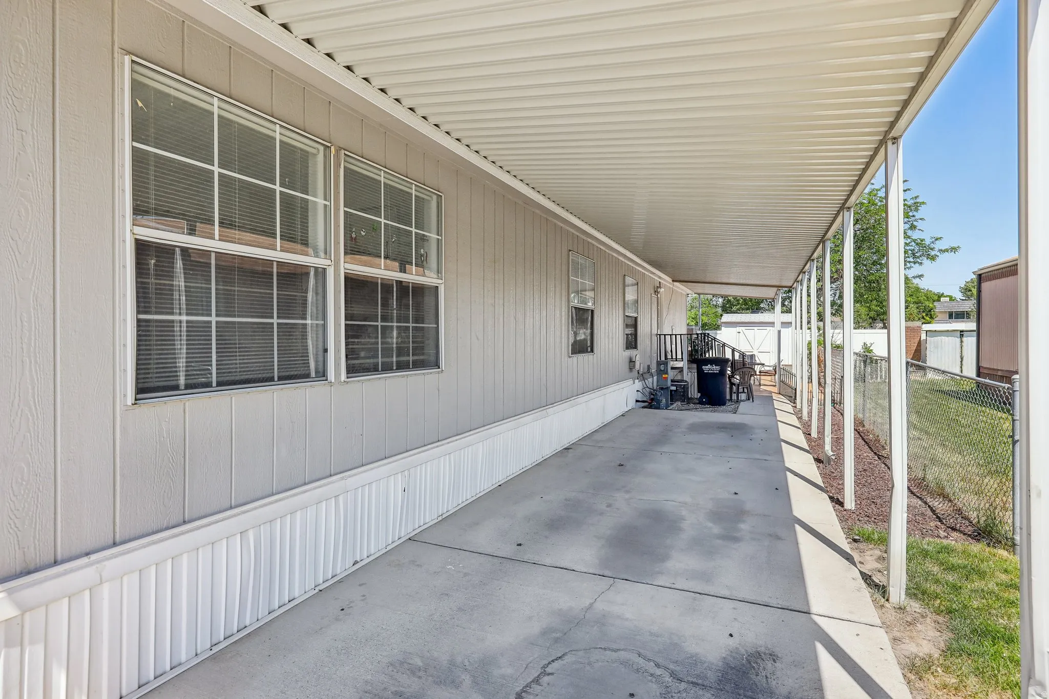 Covered concrete patio extending the length of the structure, featuring a corrugated metal roof and multiple support columns