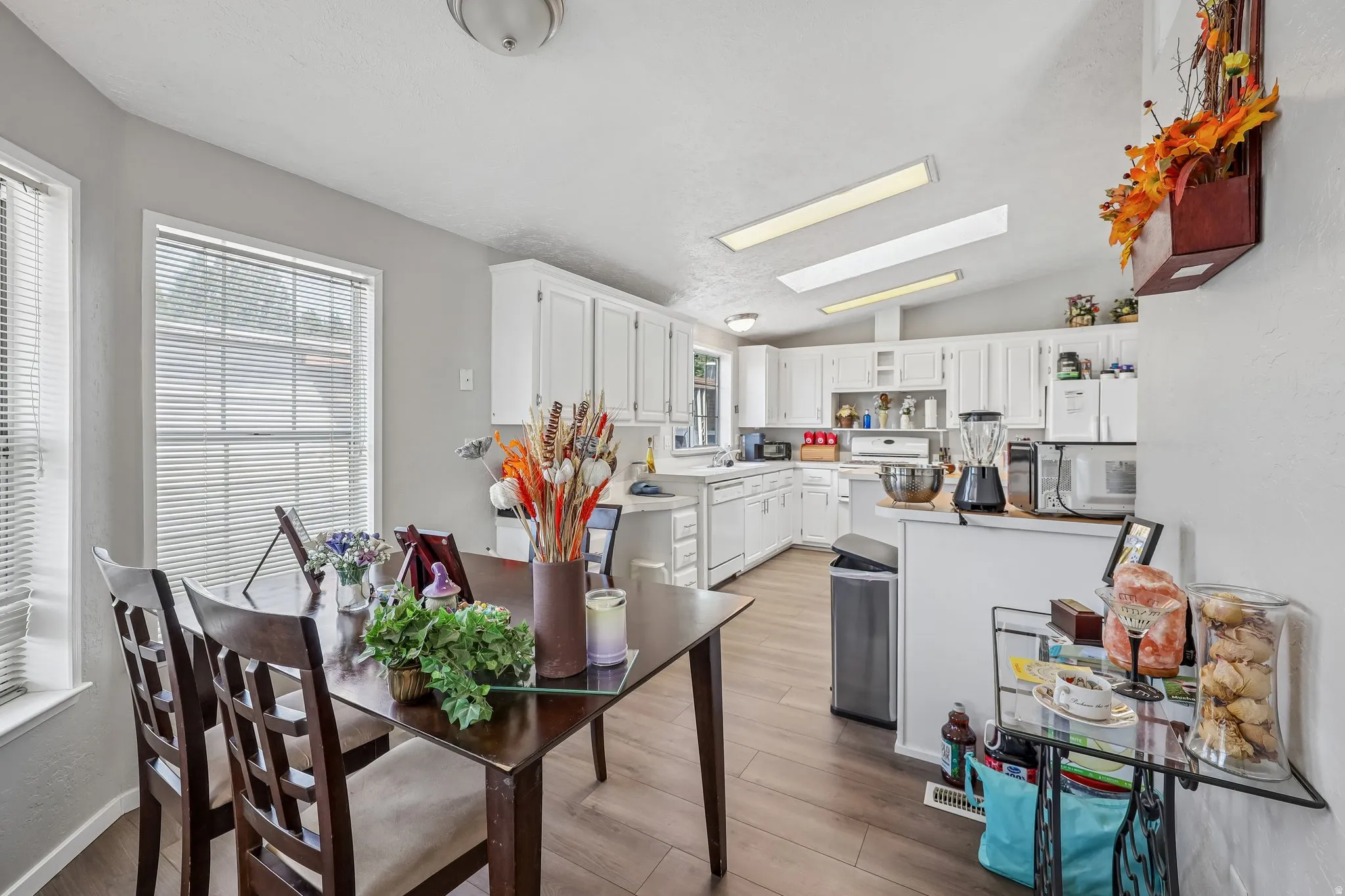 Kitchen and dining area featuring wood-finish flooring, white cabinetry, and a vaulted ceiling with integrated lighting
