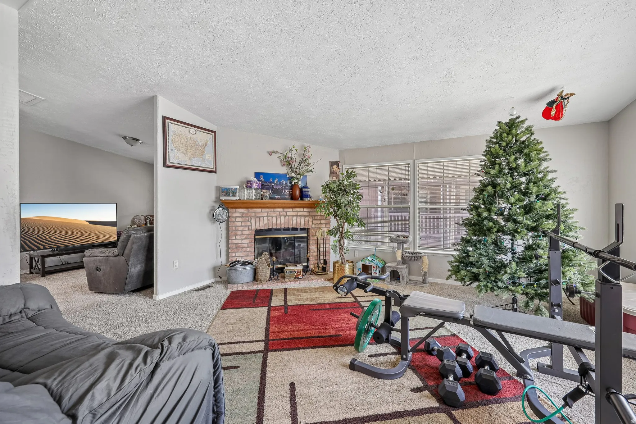 Living area featuring a brick fireplace with a wood mantle, carpet flooring, and large windows with blinds