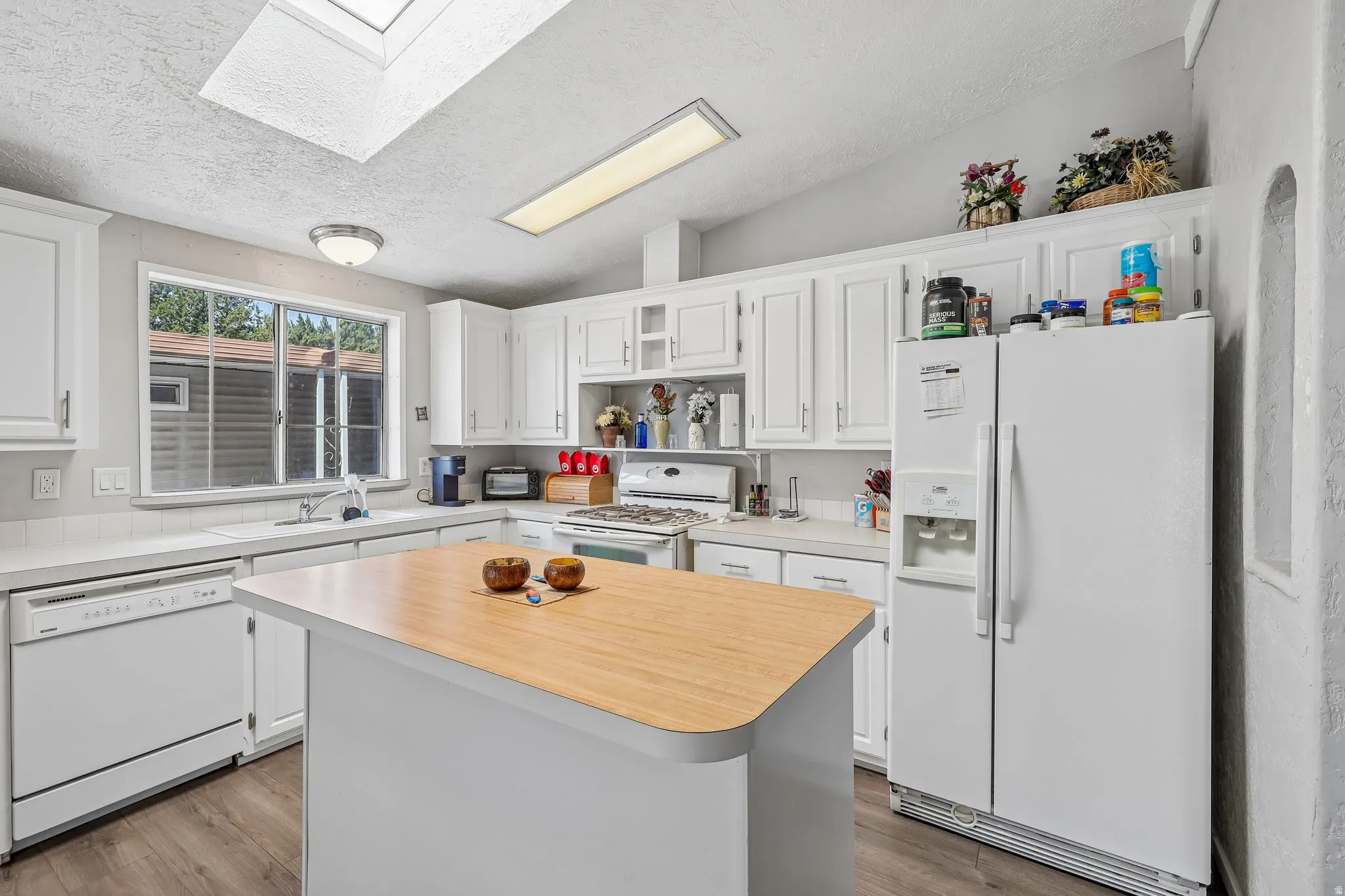 White cabinetry kitchen featuring a skylight, wood-finish flooring, central island with wood countertop, built-in dishwasher, and a side-by-side refrigerator