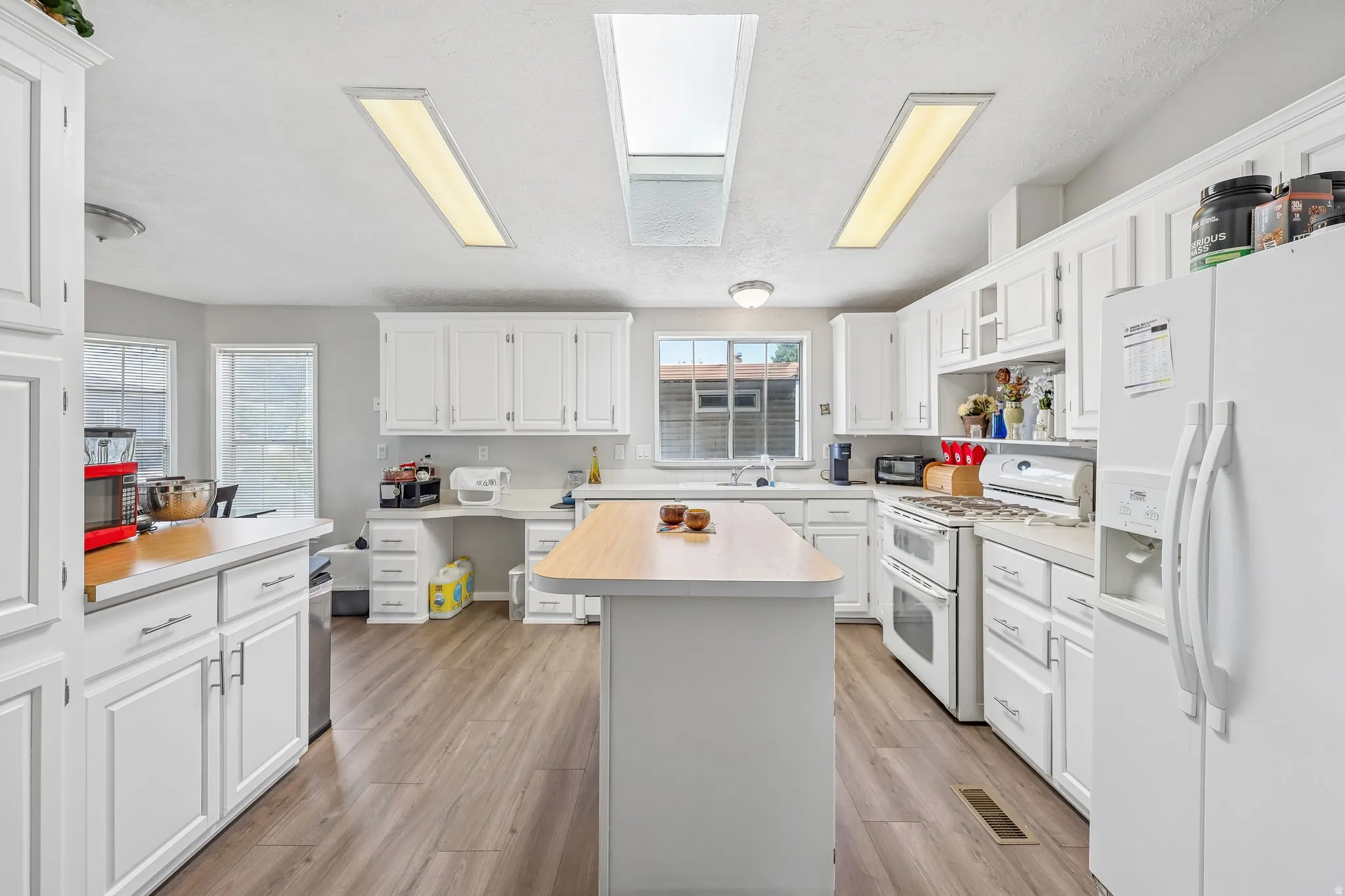 White kitchen featuring an island with a wood-finish countertop, white cabinetry with silver hardware, and wood-finish flooring