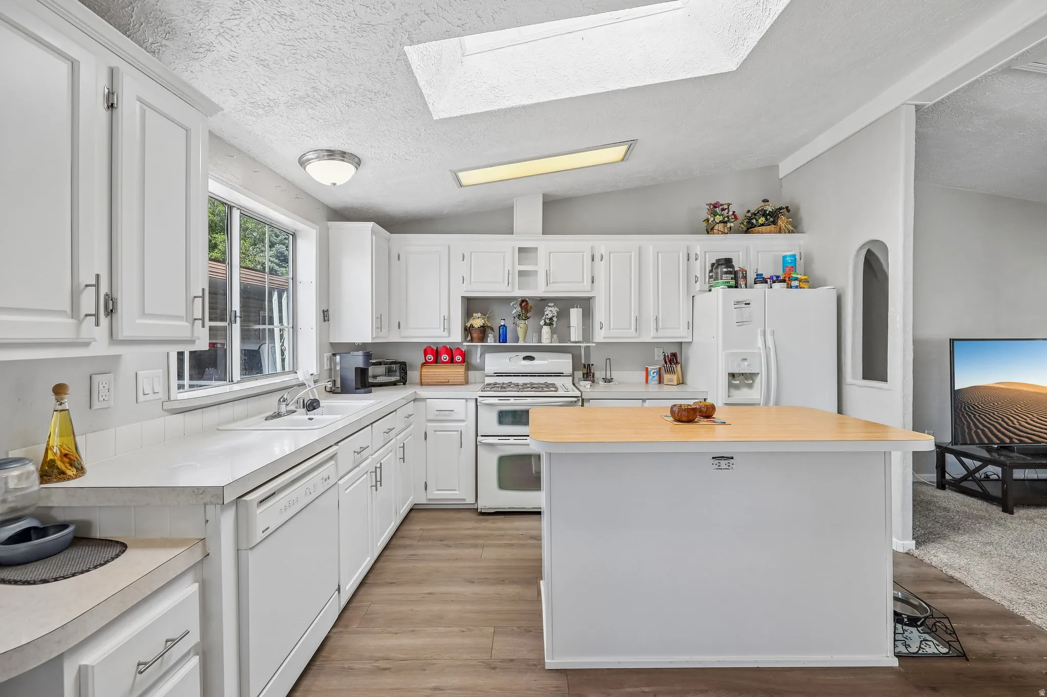Kitchen featuring white cabinetry, wood-finish flooring, white appliances, a center island with a light wood-finish countertop, and a skylight