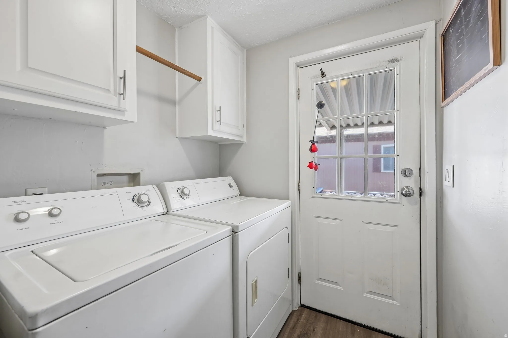 Laundry area featuring wood-finish flooring, white cabinetry with silver hardware, a built-in hanging rod, and a white exterior door with a window pane