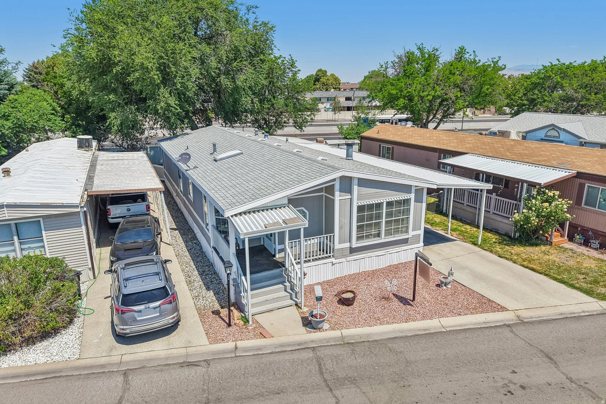 Light gray mobile home featuring a covered front entry and a gravel landscaping bed