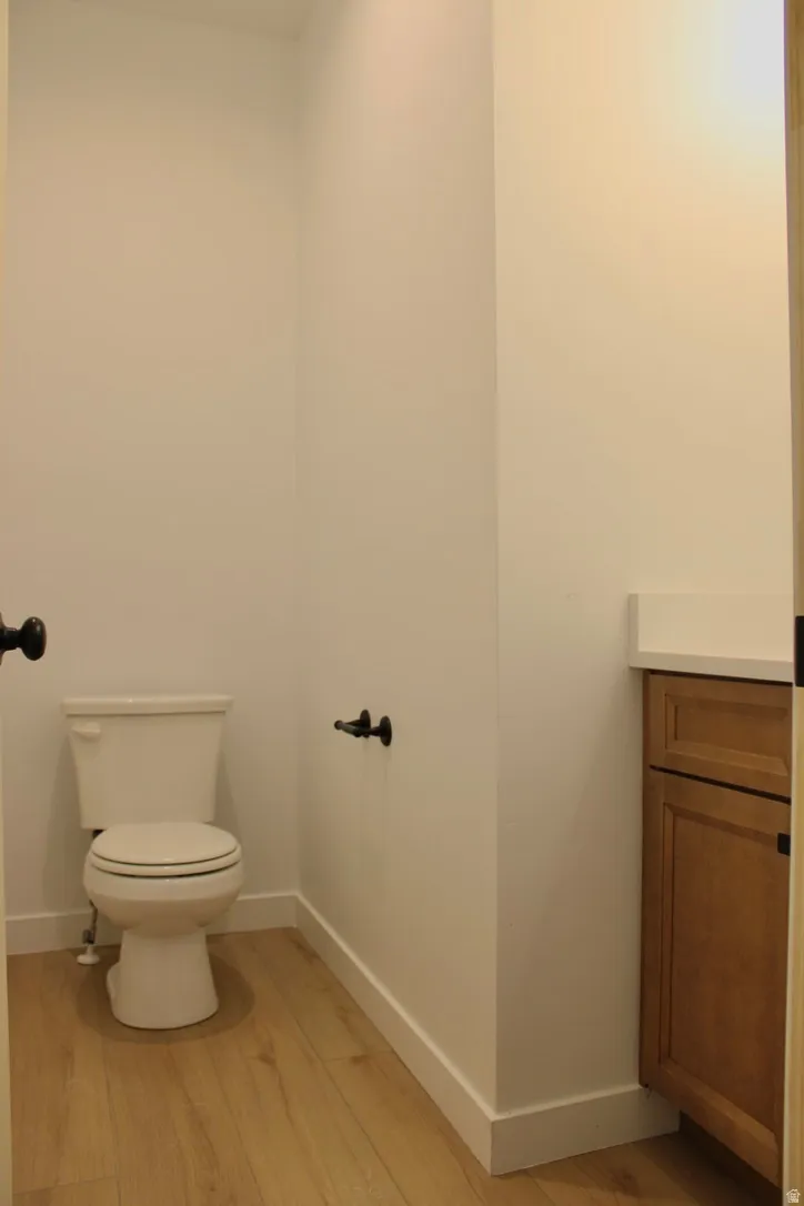 Powder room featuring wood-finish flooring, a white toilet, and a vanity with a light-colored countertop and wood-finish cabinetry