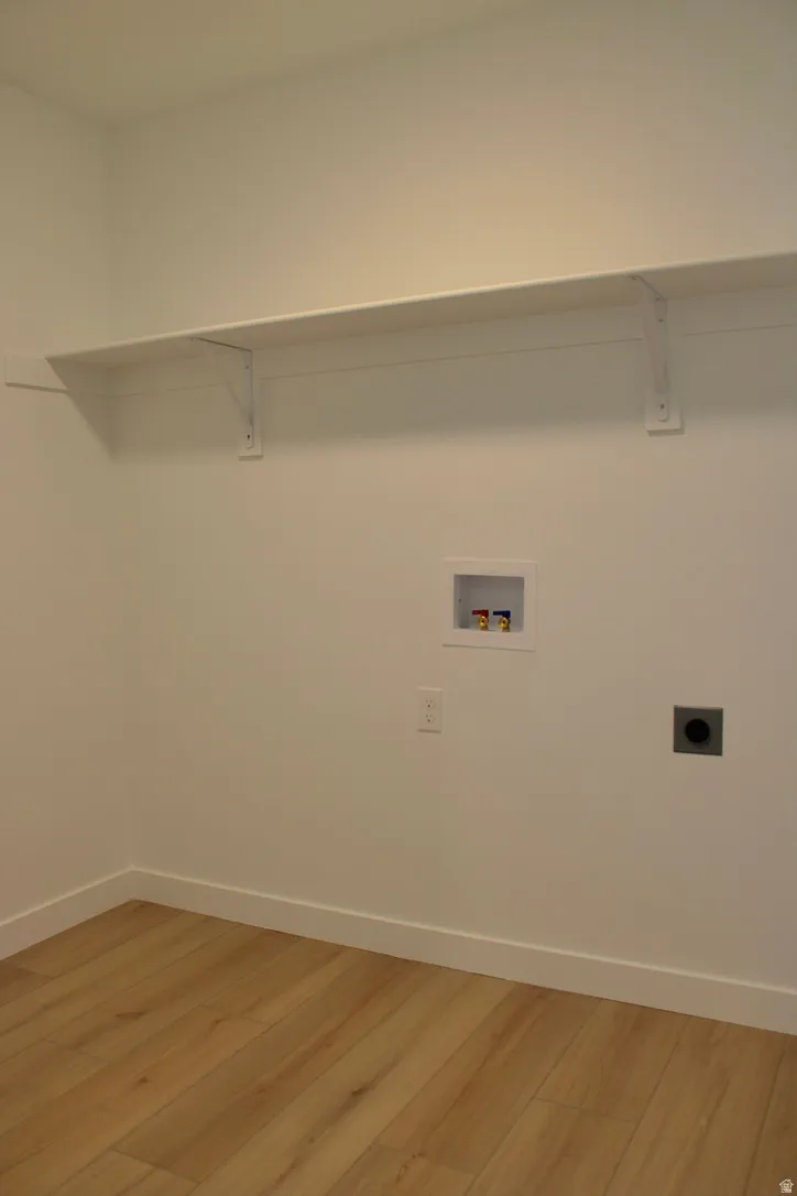 Utility room featuring wood-finish flooring, white walls, and a white storage shelf