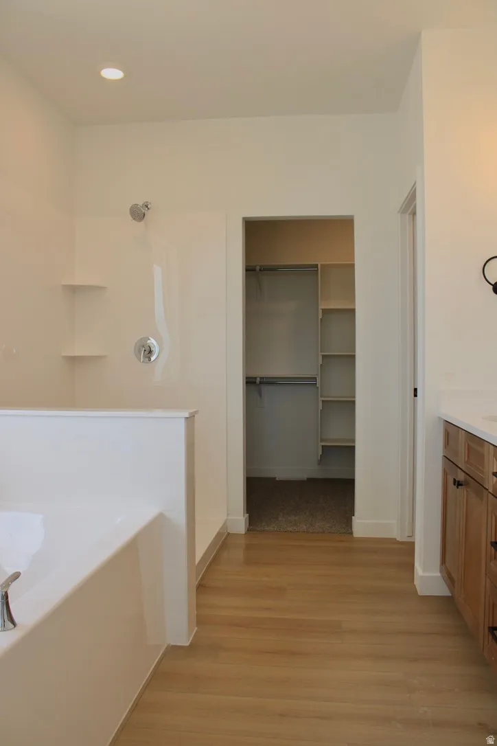 Spacious bathroom featuring a built-in tub, separate shower with chrome fixtures, wood-finish flooring, recessed lighting, and a walk-in closet with built-in shelving