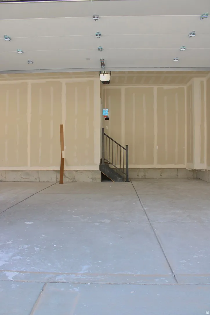 Spacious garage with concrete flooring, unfinished drywall, and an integrated staircase featuring a black metal railing