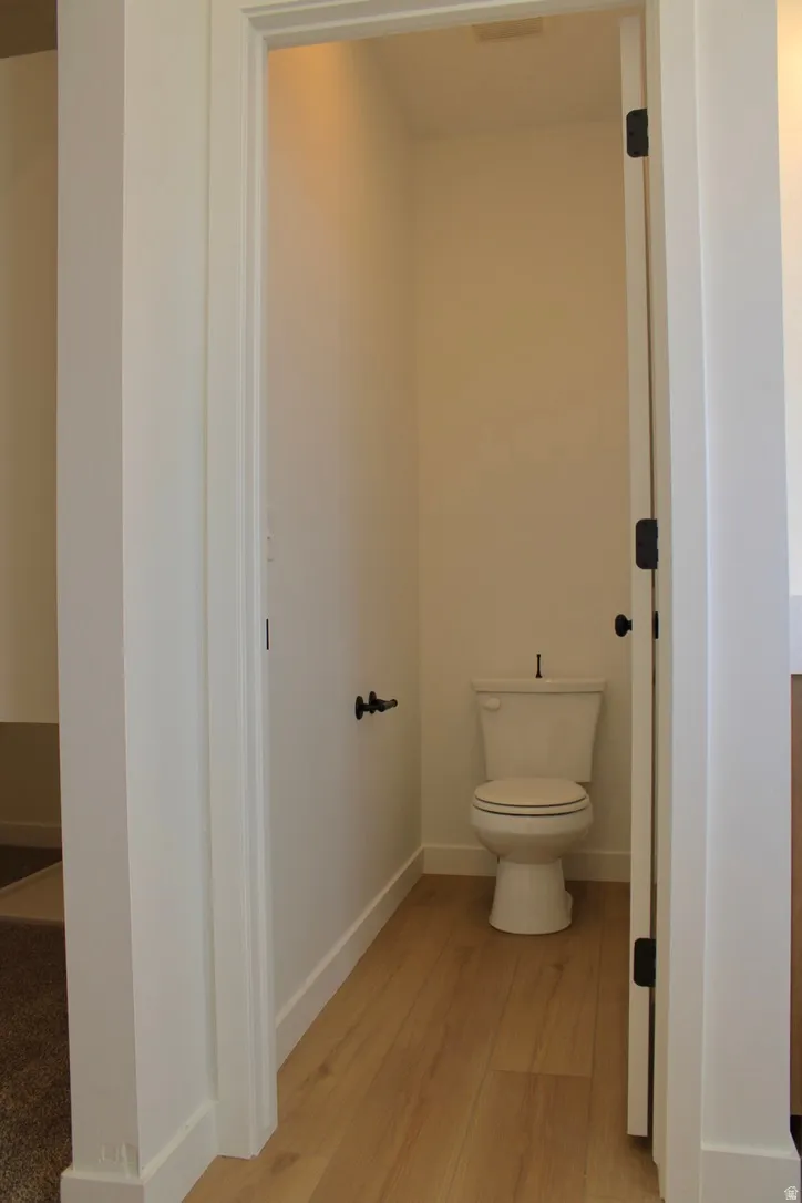Powder room featuring light wood-finish flooring, a white toilet, and contrasting dark hardware