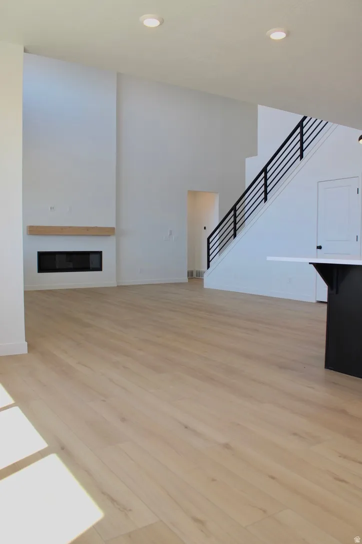 Spacious living area featuring wood-finish flooring, a contemporary fireplace with a wood mantle, and a modern staircase with black railings