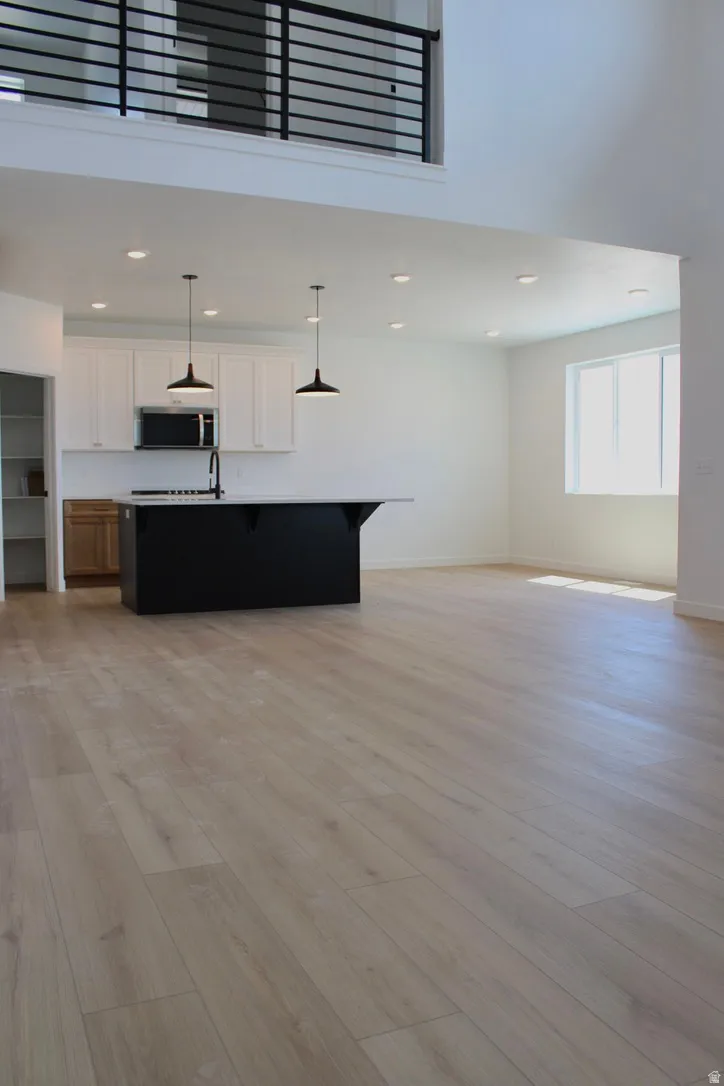 Open-concept living area featuring light wood-finish flooring, a two-story ceiling, and a modern black railing on the upper level