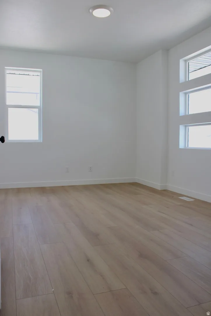 Spacious room featuring light wood-finish flooring, white walls, and bright overhead lighting