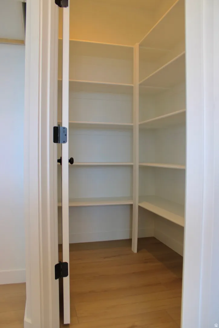 Walk-in pantry featuring white shelving, wood-finish flooring, and a white paneled door with black hardware
