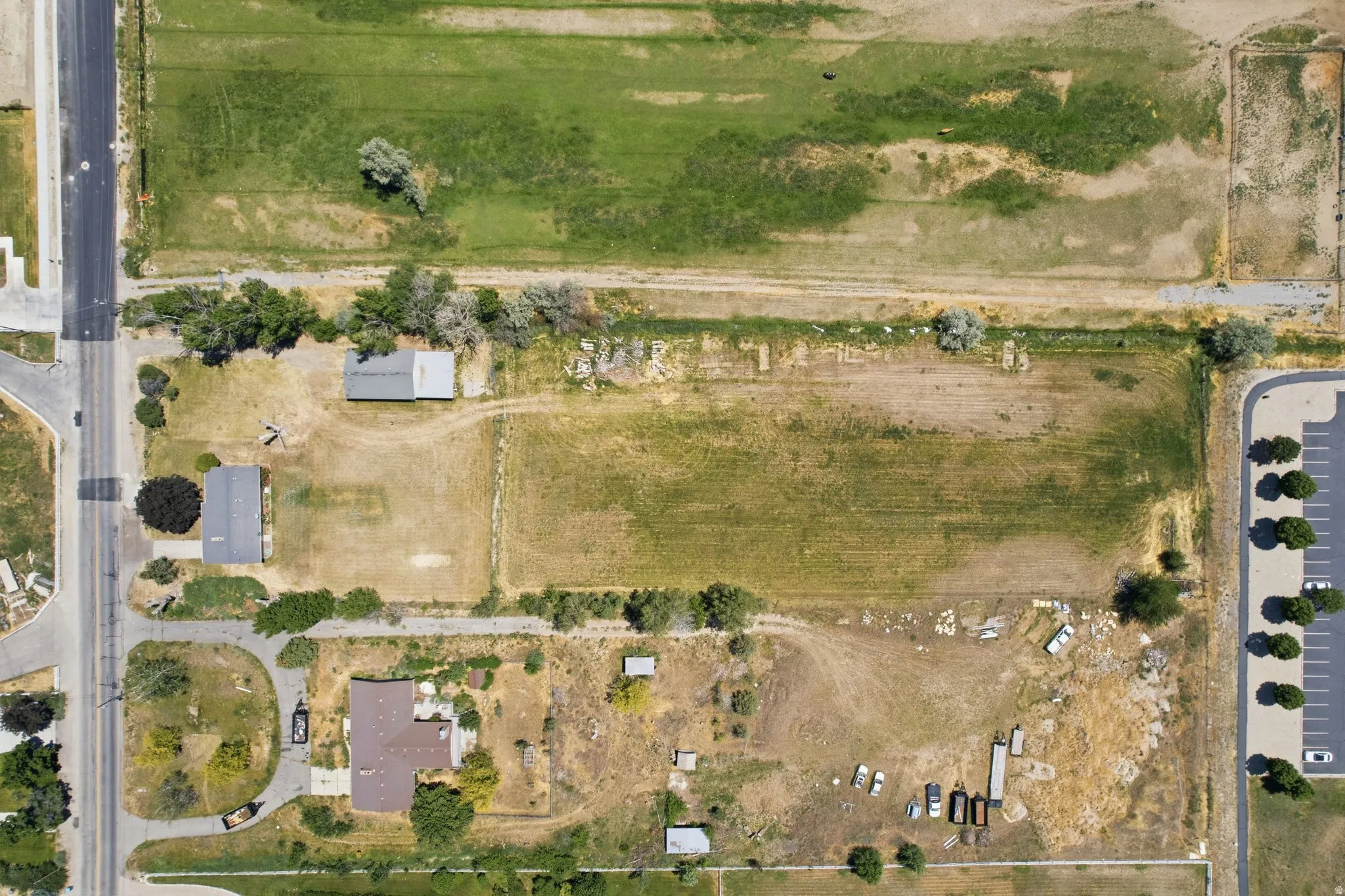 Expansive property featuring a large undeveloped parcel, two separate structures with dark-toned roofs, mature trees, and direct road frontage