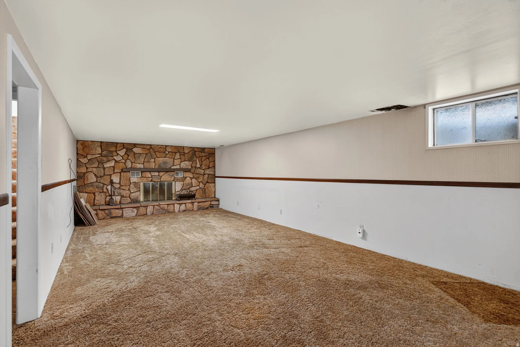 Spacious room featuring a stone-clad fireplace with a hearth and a metal screen, plush carpeting, and wainscoting with a wood trim