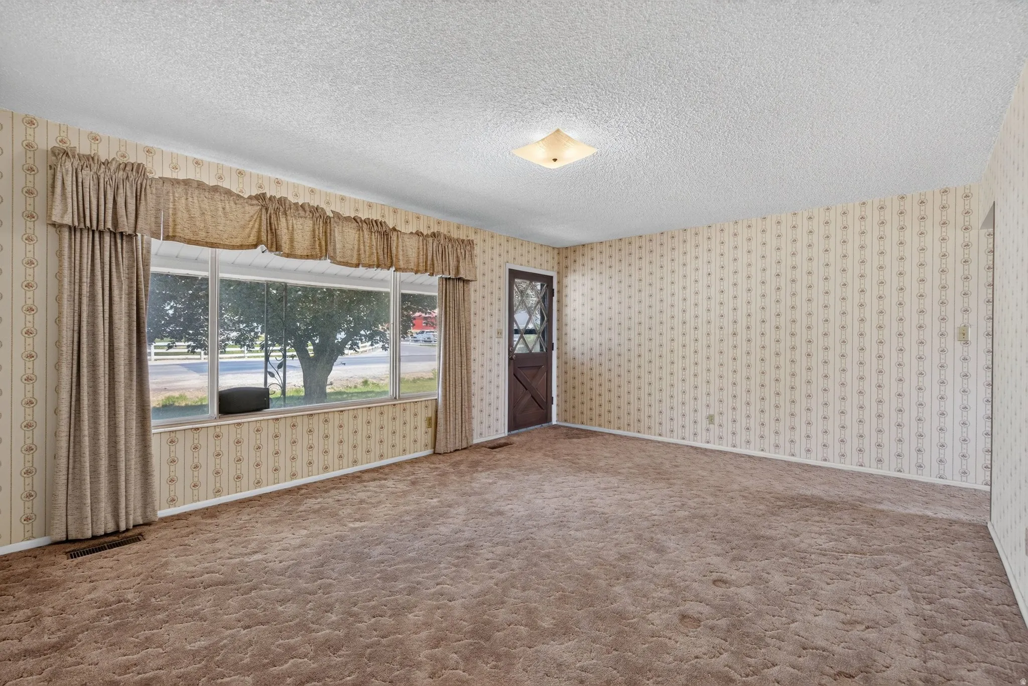 Spacious room featuring patterned wallpaper, textured ceilings, and wall-to-wall carpeting