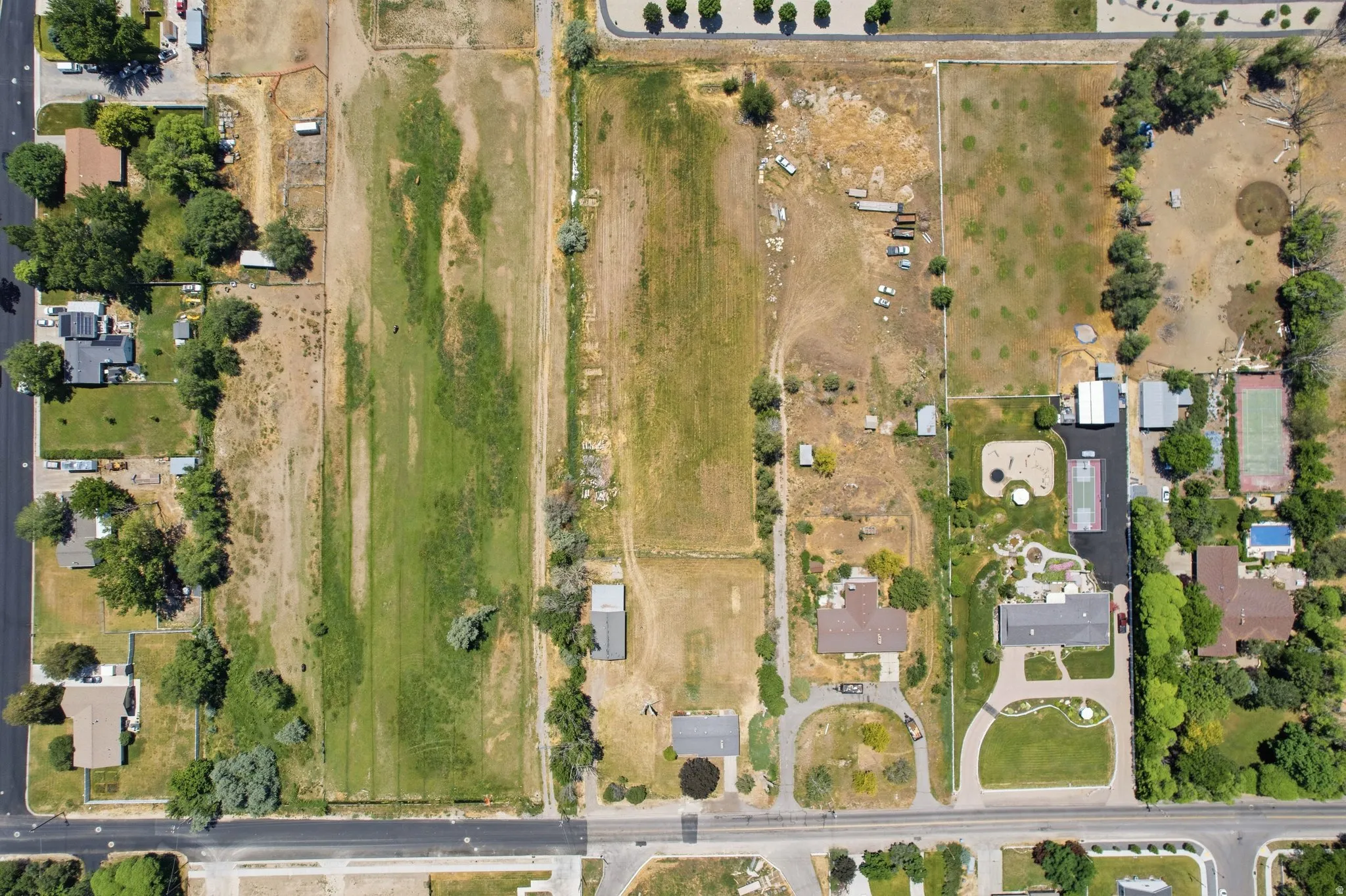 Expansive land parcel featuring existing residential properties, undeveloped terrain, and mature trees