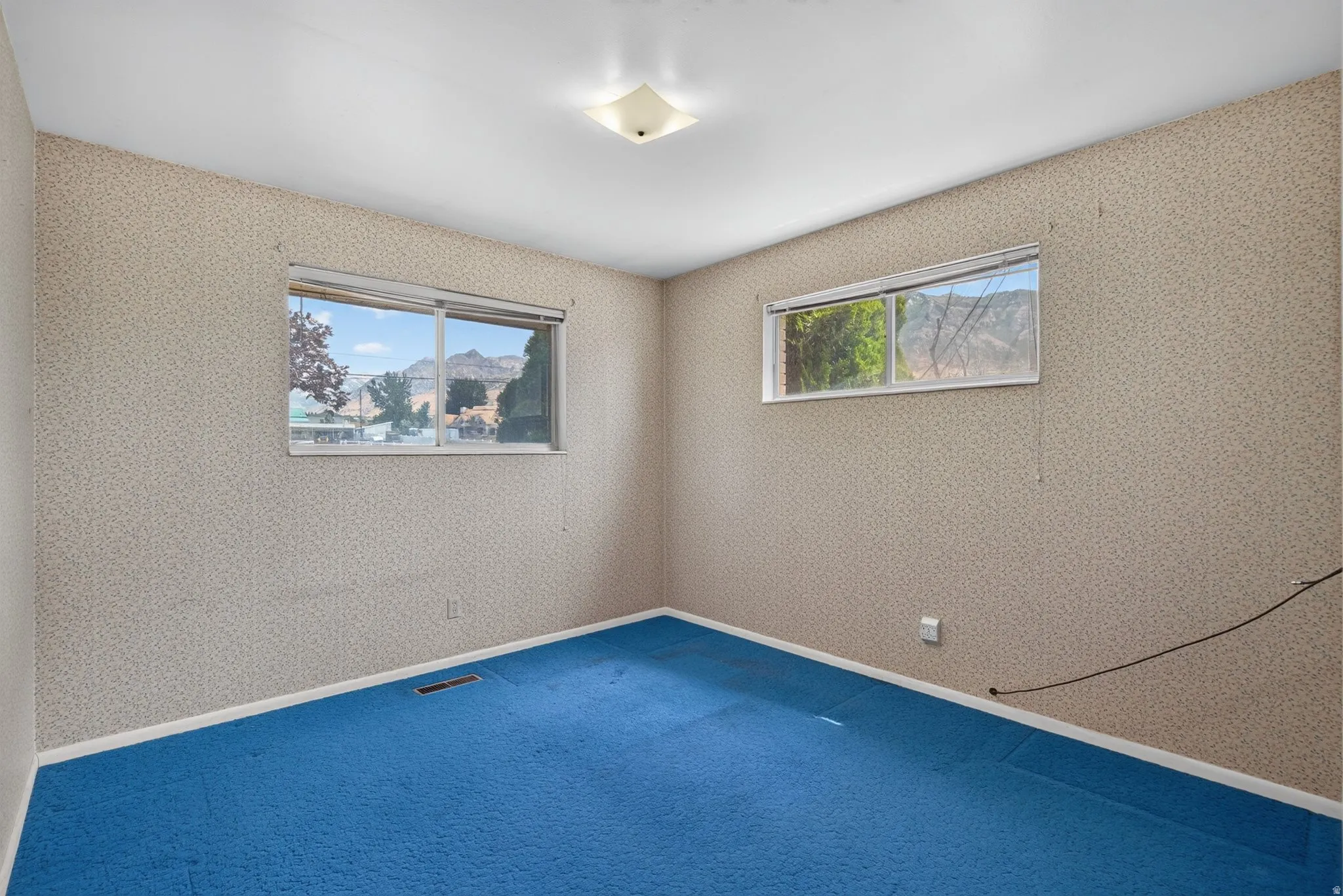 Room featuring two large windows, blue carpeting, and patterned wallpaper