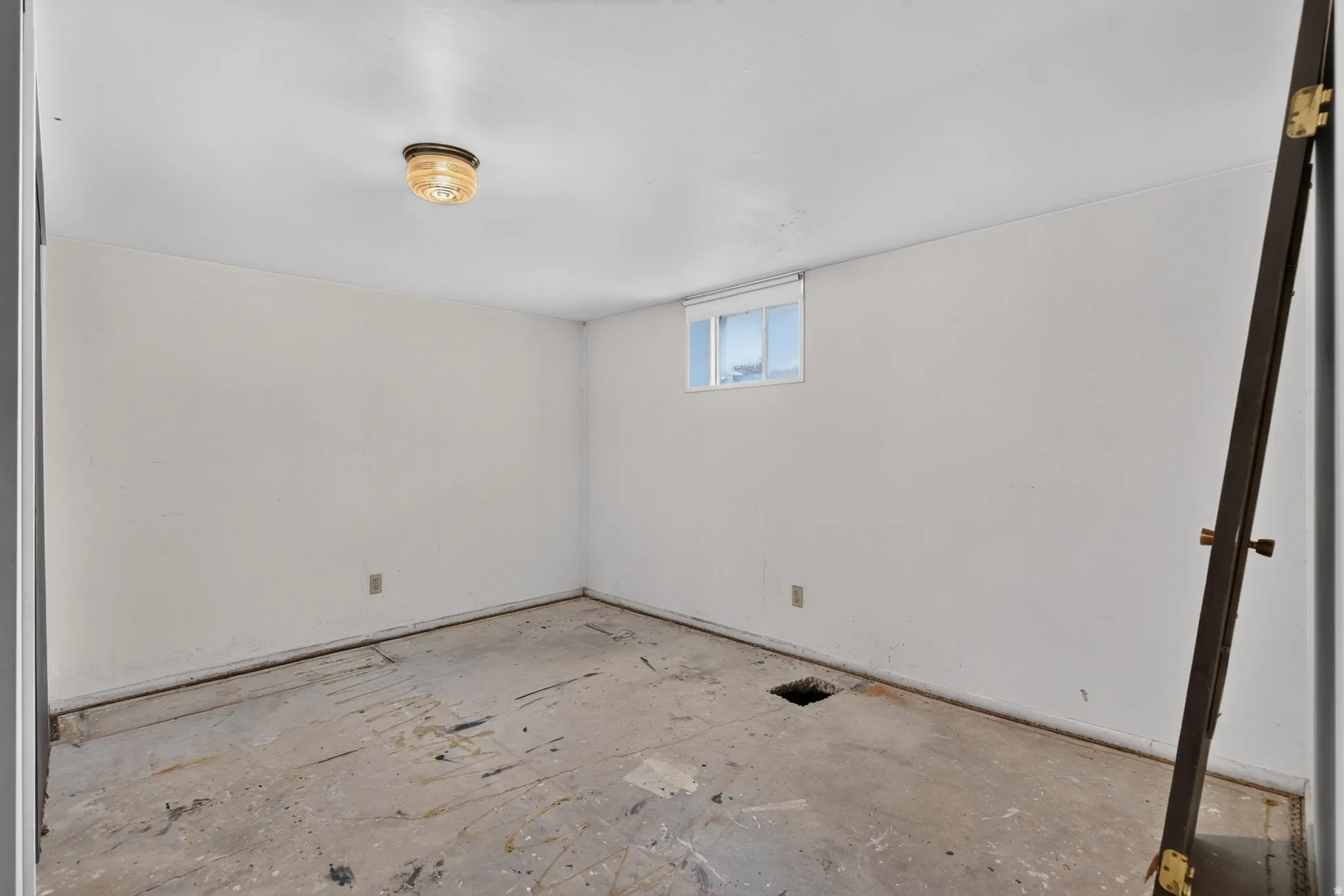 Room featuring a window, ceiling-mounted light fixture, white walls, and exposed subfloor