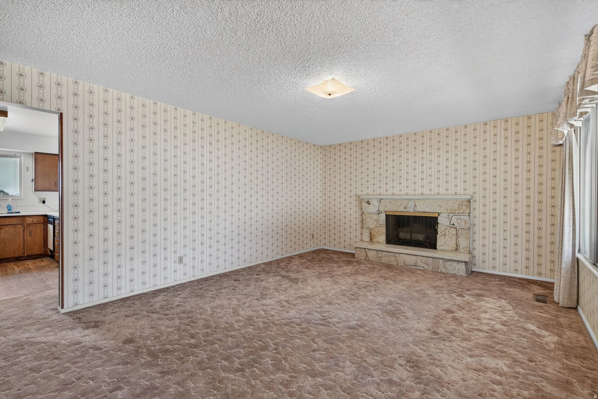 Living area featuring a stone fireplace with hearth, textured carpeting, patterned wallpaper, and a flush-mount ceiling light fixture
