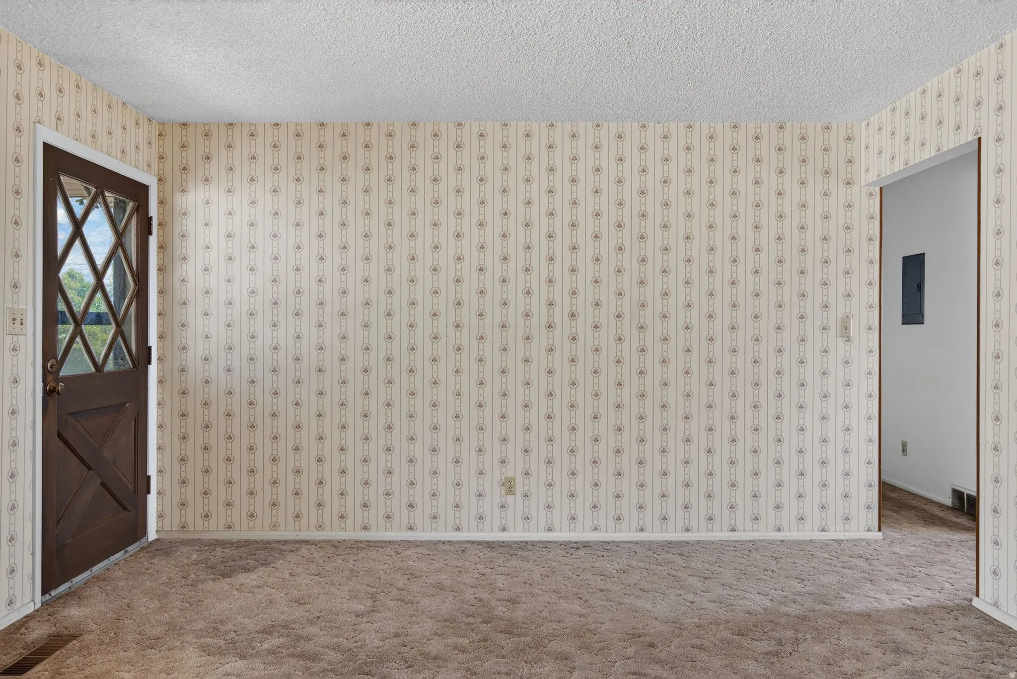 Entryway featuring a diamond-paneled dark wood door, patterned wallpaper, textured ceiling, and brown carpet