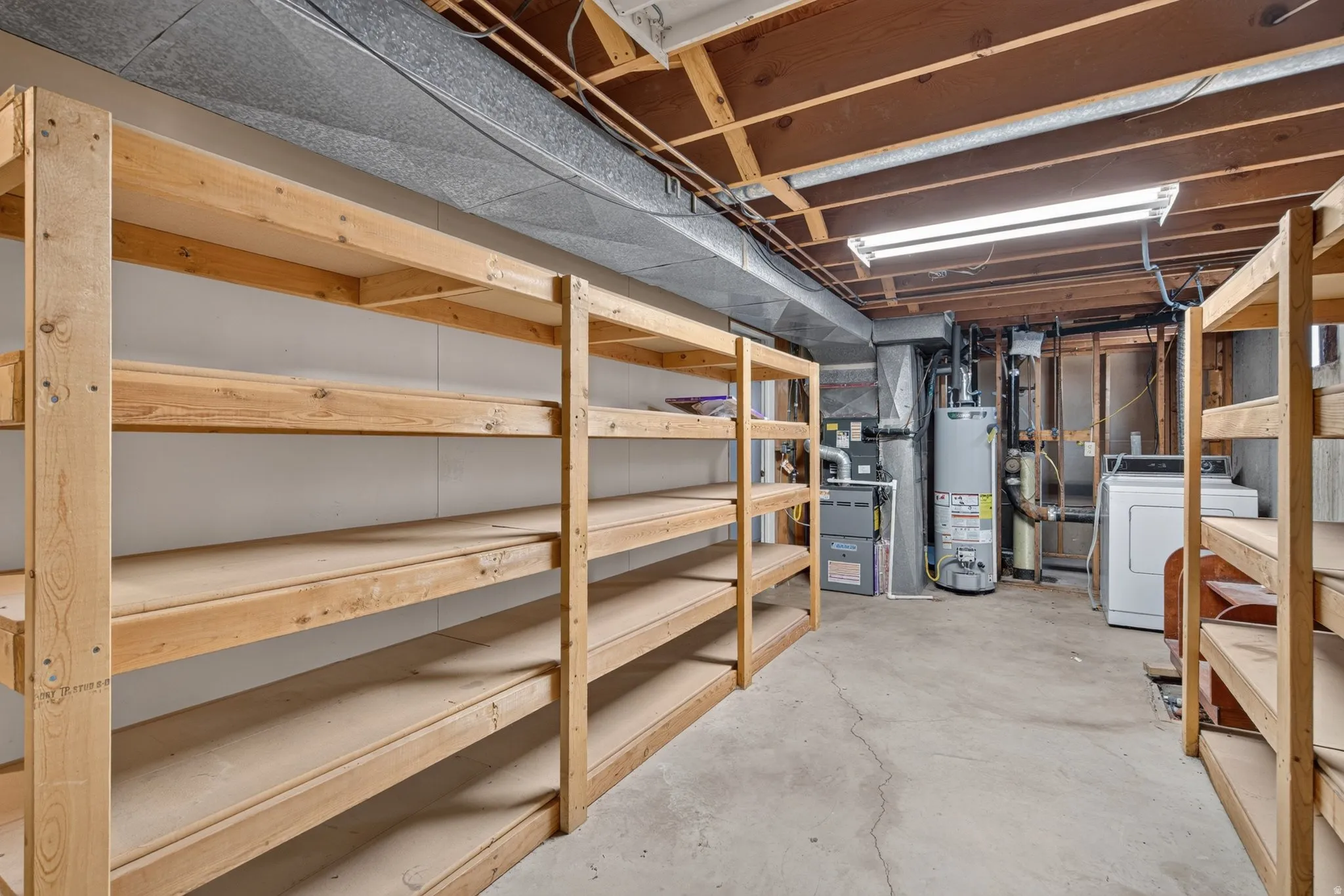 Basement storage area featuring extensive wood shelving, concrete flooring, exposed ceiling joists, and fluorescent lighting