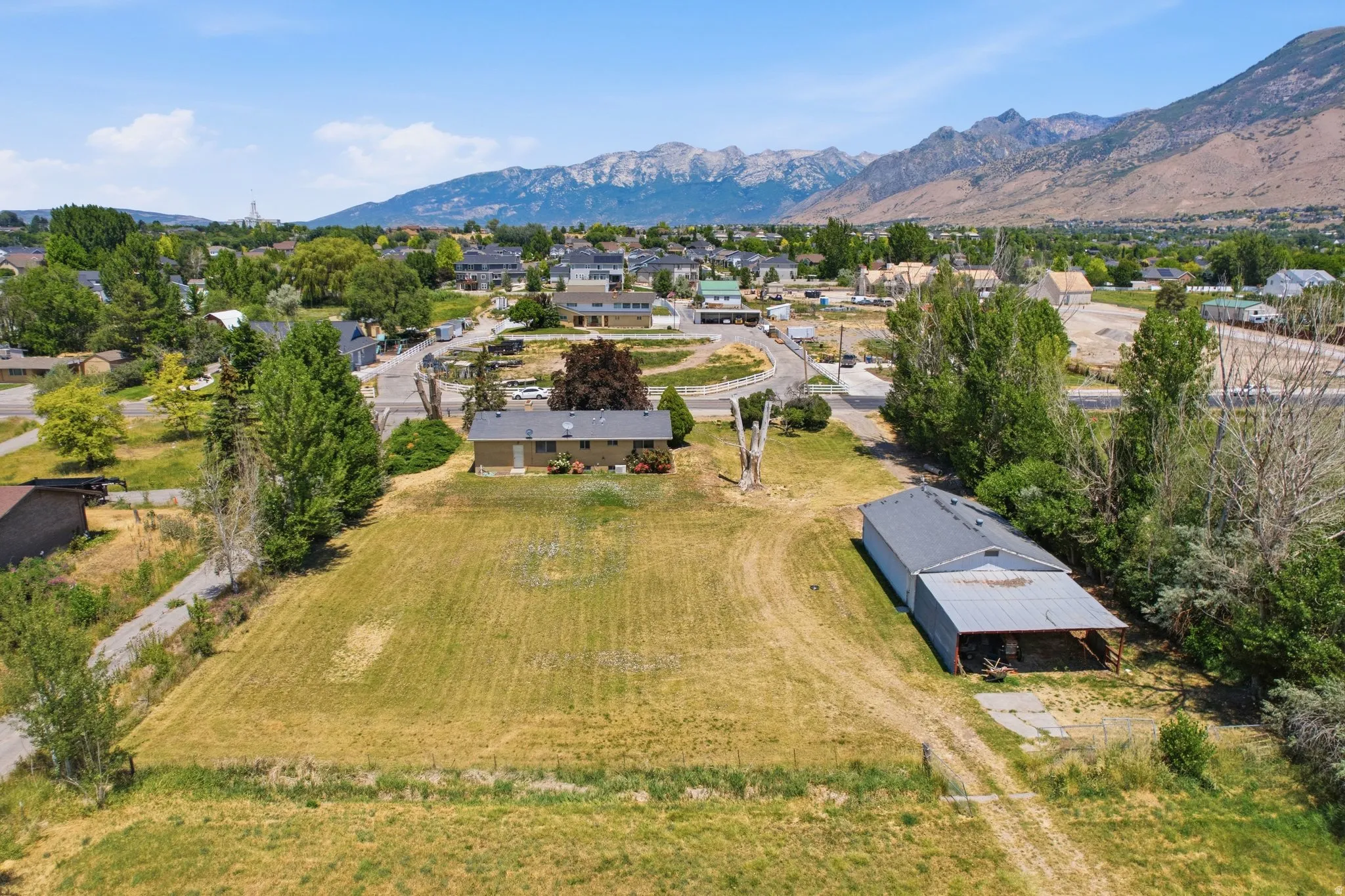 Expansive undeveloped land featuring a detached residential structure, a large outbuilding, mature trees, and a mountainous backdrop